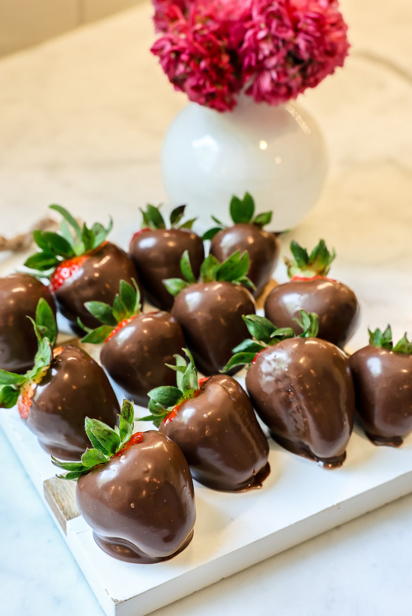 Chocolate dipped strawberries on a white tray with pink flowers in the background