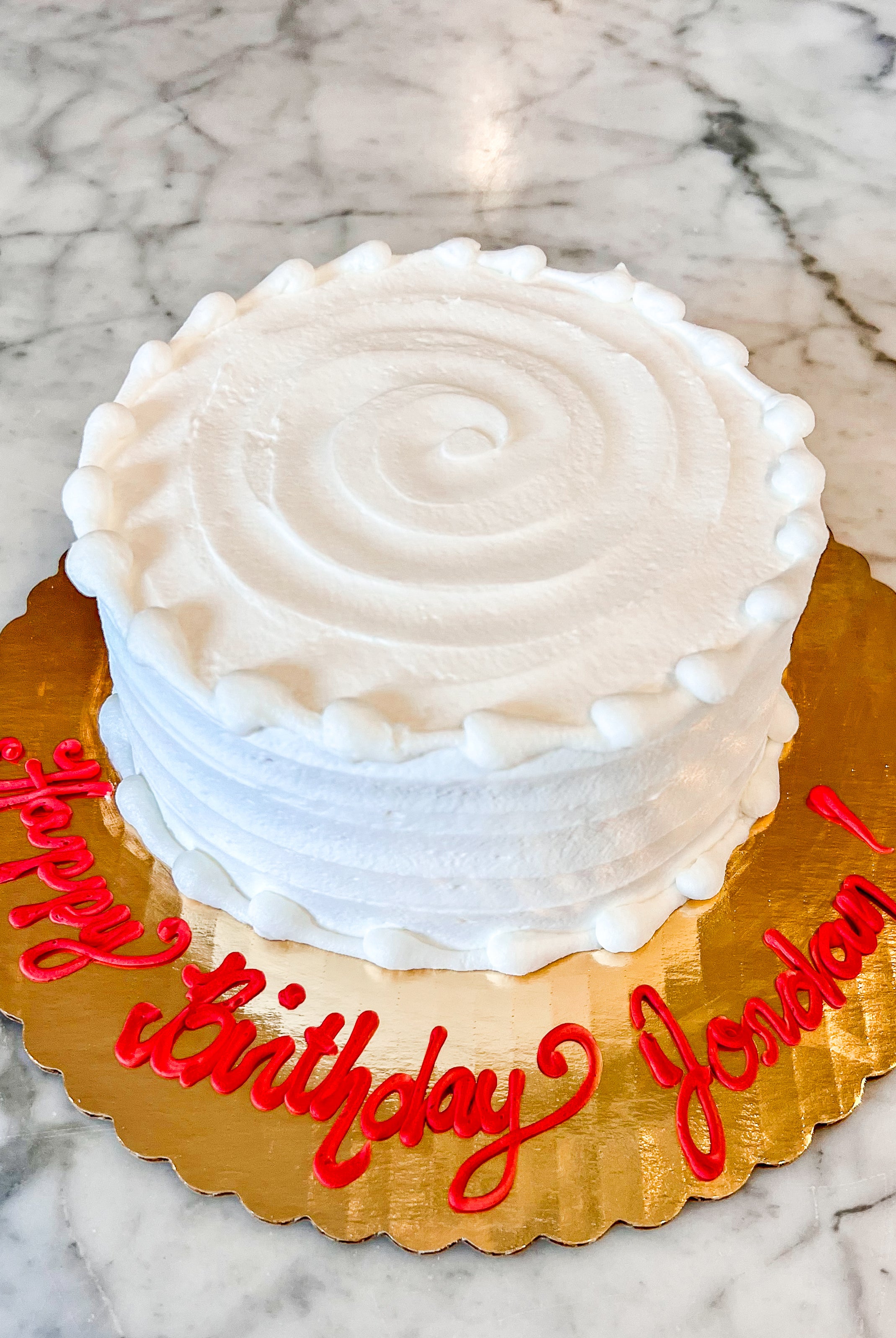Cake with white icing on a gold platter with red writing "Happy birthday Jordan!"
