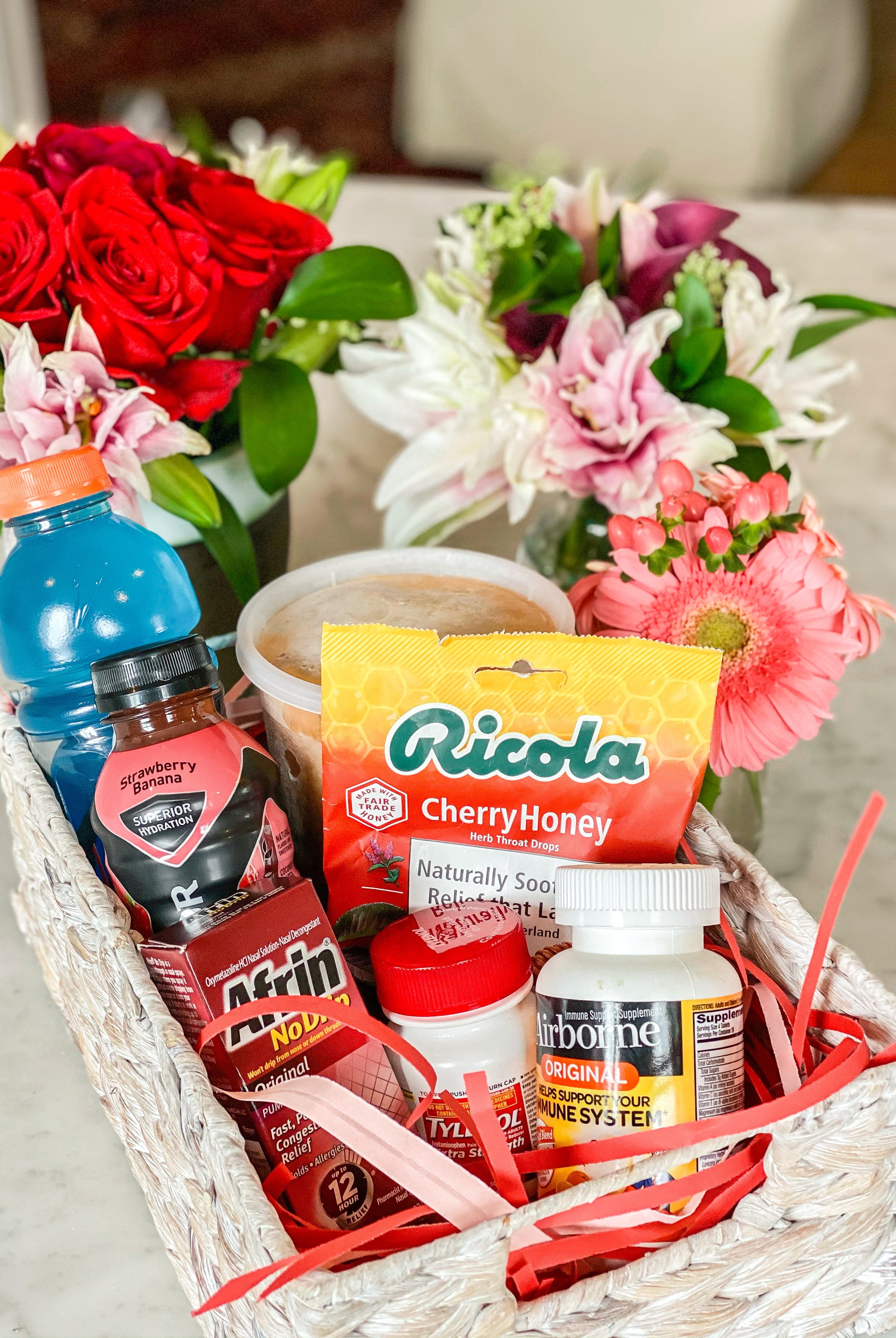 Basket of get well soon goodies, including gatorade, medicine, soup, and flowers