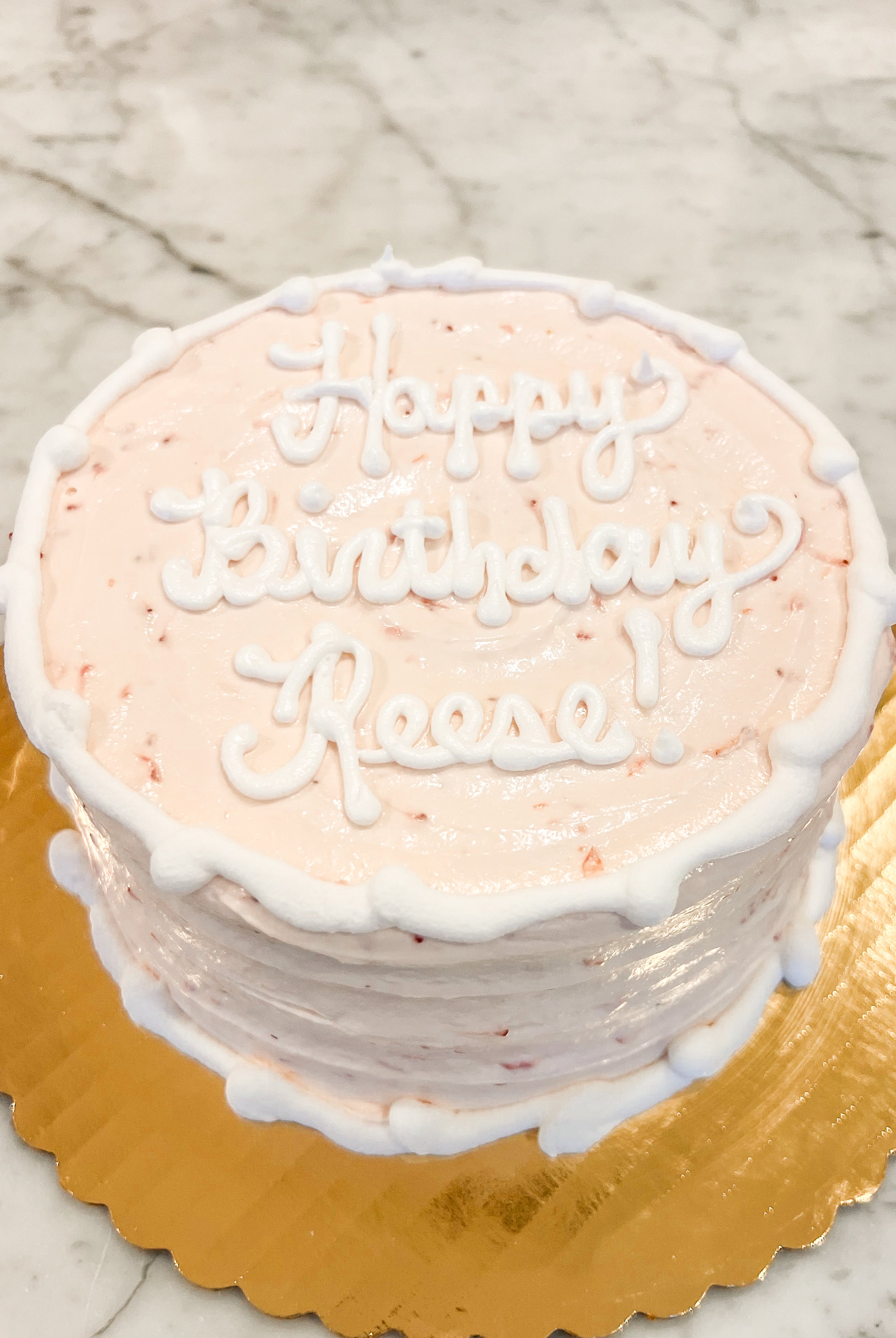 Strawberry cake with white icing that says "Happy birthday Reese!" on a gold platter