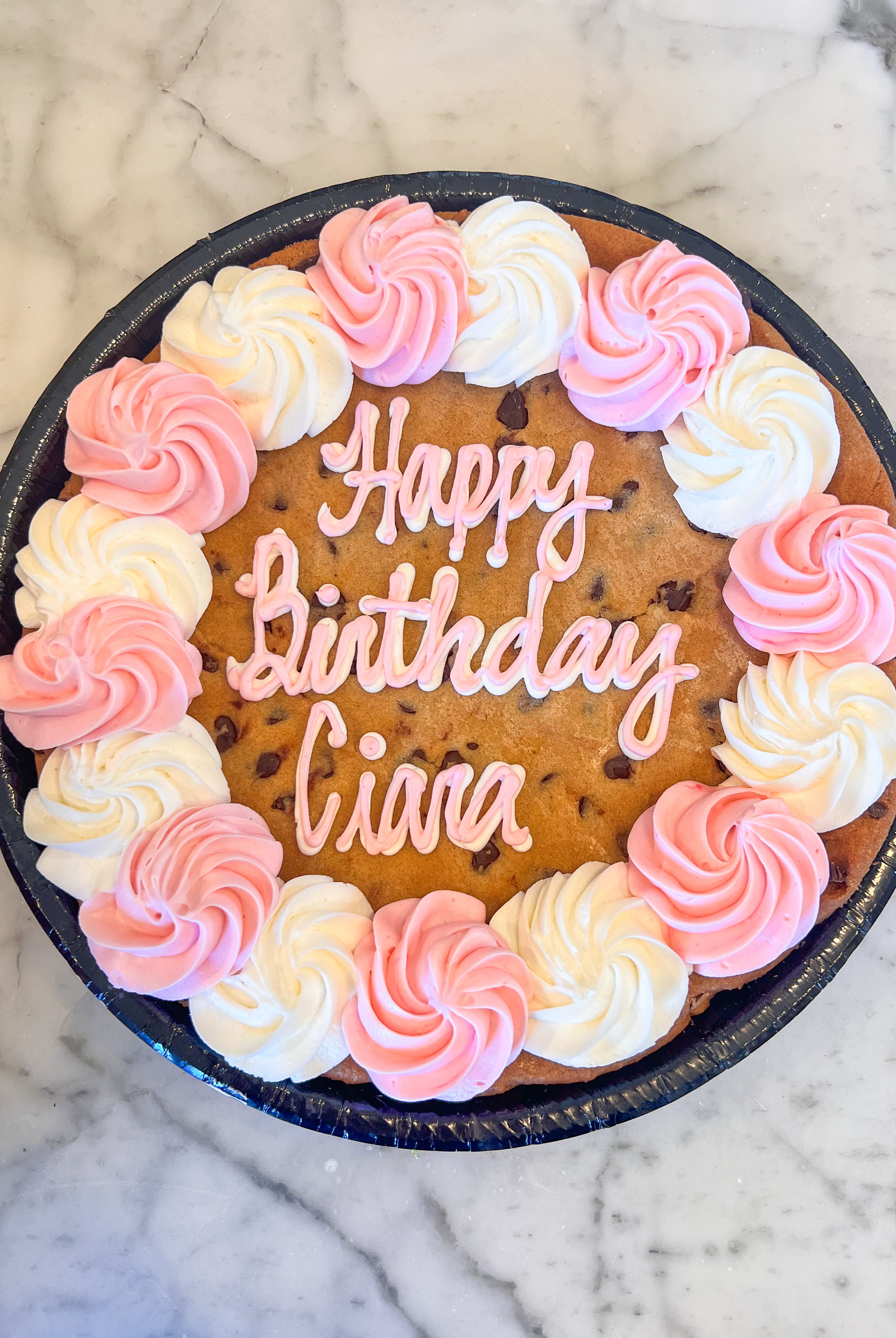Cookie cake with white and pink icing that says "Happy birthday Ciara"