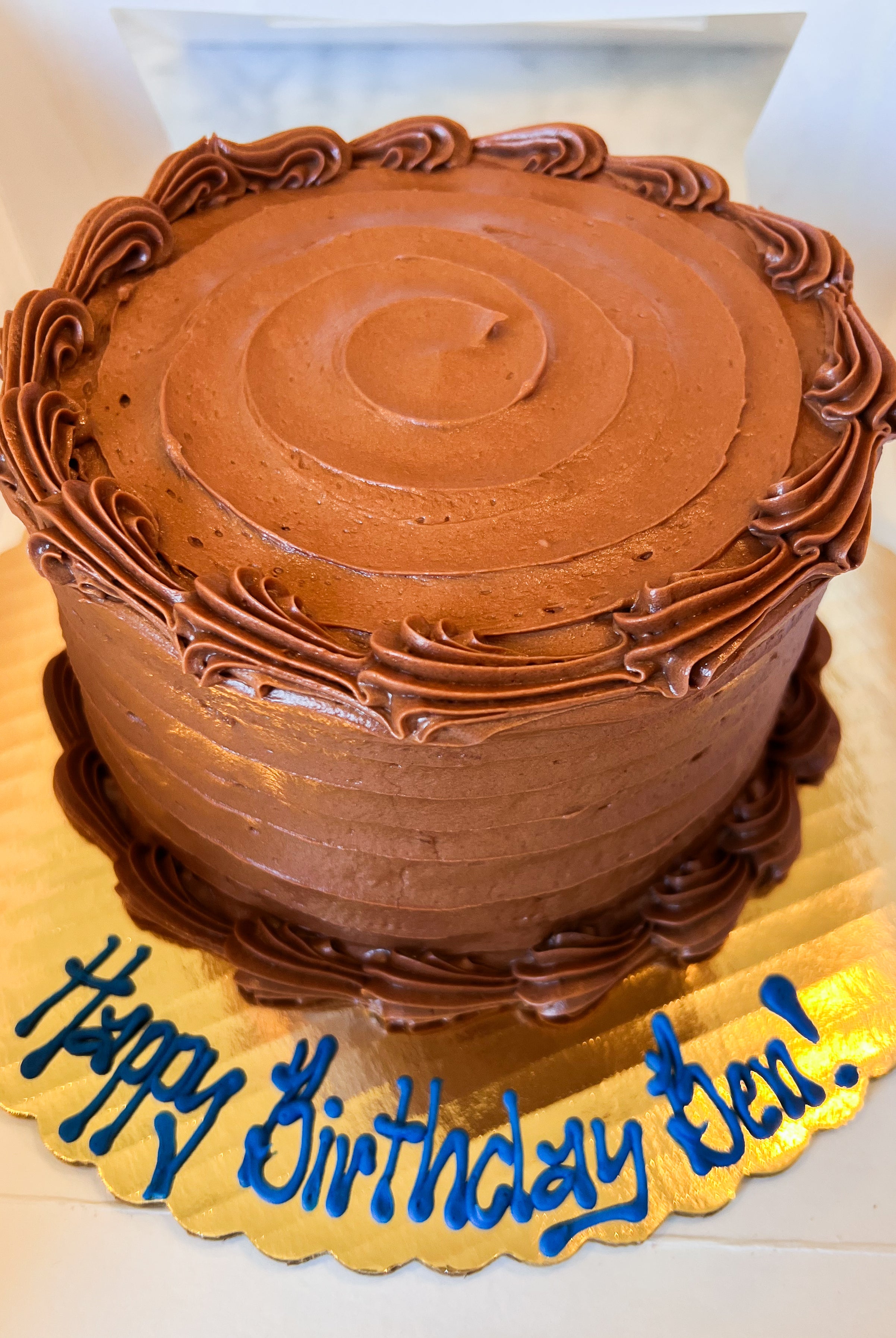 Chocolate cake on a gold platter with blue icing that says "Happy birthday Ben!"