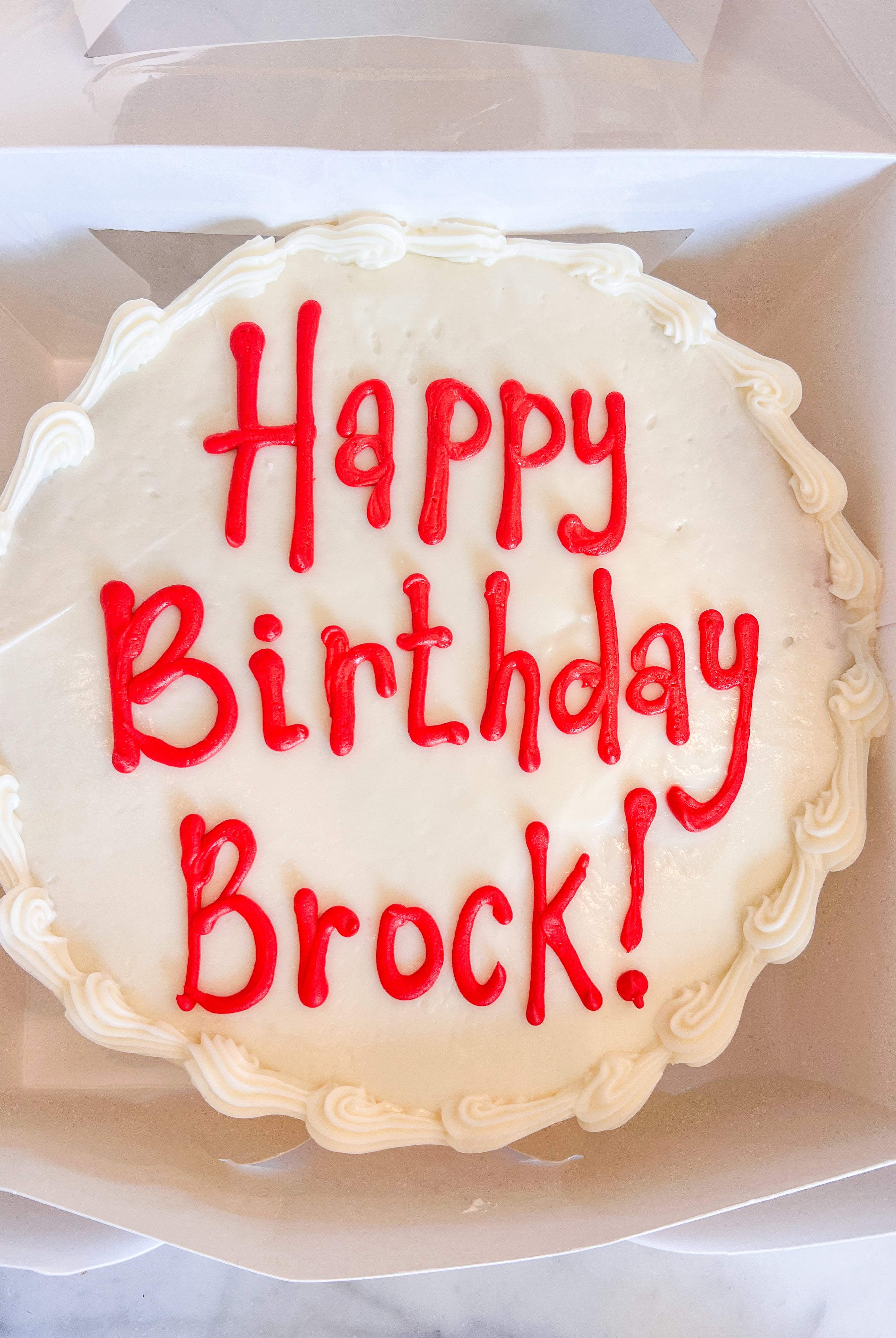 Cake with white icing that says "Happy Birthday Brock!" in red icing
